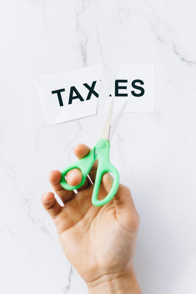 pexels photo 6863325 6863325 Top-down view of a hand holding scissors cutting the word 'taxes' on a marble surface.