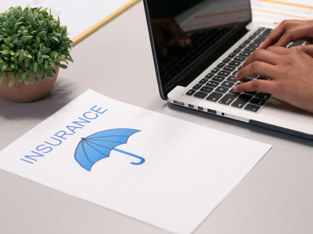 pexels photo 7688374 7688374 Close-up of hands typing on laptop with an insurance document visible on the desk.